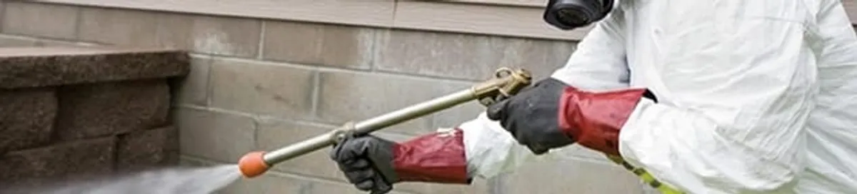 Pest control technician applying exterior insect treatment along a home foundation in Syracuse, NY