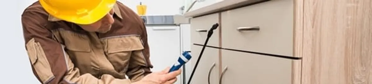 Roach exterminator applying treatment under kitchen cabinets in Syracuse, NY
