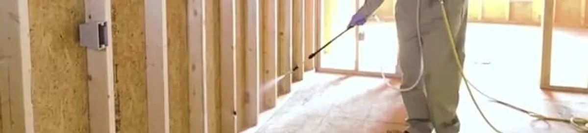 Termite treatment technician applying spray along framing and unfinished walls in Syracuse, NY
